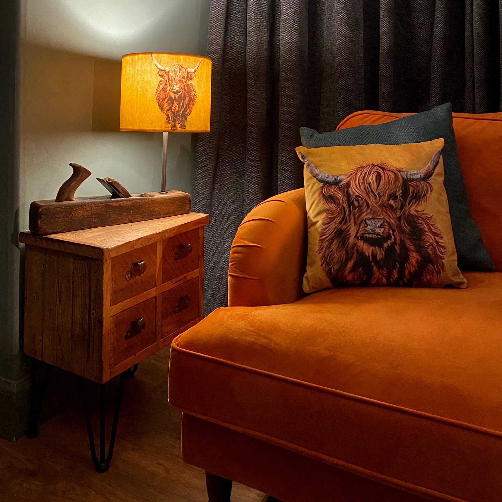 Lounge setting with soft velvet printed cushion and matching printed lampshade . Both printed with aHighland cow, mustard yellow background with rusty brown cow.